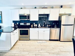 A modern kitchen with white cabinets, stainless steel appliances, a tiled backsplash, and a wooden floor. - Sunset By The Sea • Entire Property • 4BR/2BA • Pool & Swim (Fort Myers Beach)