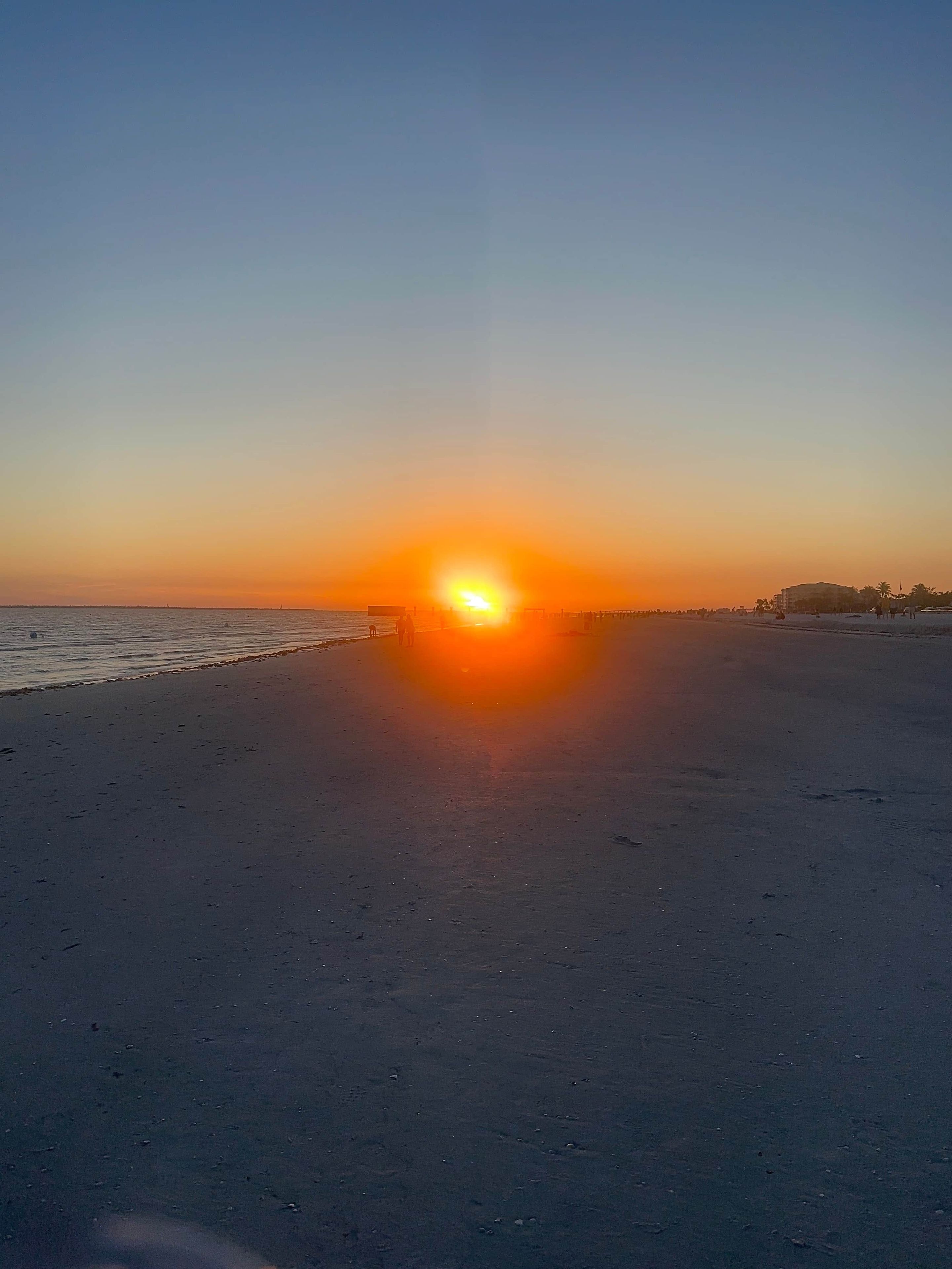 A beach at sunset with a pier extending into the water.