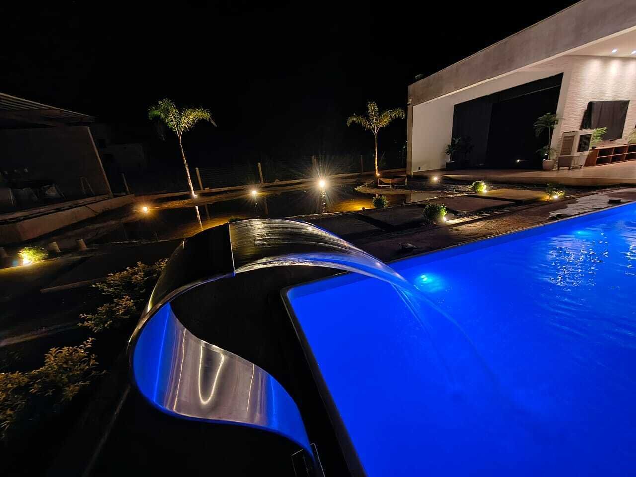 Una piscina de borde curvo, rodeada por un área ajardinada con plantas pequeñas y un edificio moderno al fondo.