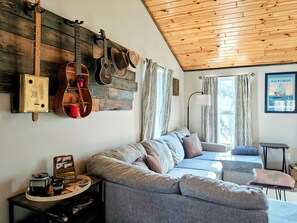 A cozy living area with a wooden ceiling, a sofa, a coffee table, and a wall-mounted guitar rack.