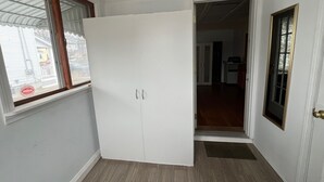 Ein Zimmer mit einem weißen Schrank, einem Fenster mit Blick ins Freie und einer Tür zu einem anderen Raum.