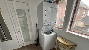 Ein Waschraum mit einer Waschmaschine und einem Trockner mit Frontlader, Holzboden, einer Tür mit Fensterglas und einem kleinen Tisch mit floralem Muster.