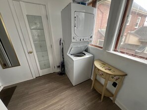 Ein Waschraum mit einer Waschmaschine und einem Trockner mit Frontlader, Holzboden, einer Tür mit Fensterglas und einem kleinen Tisch mit floralem Muster.