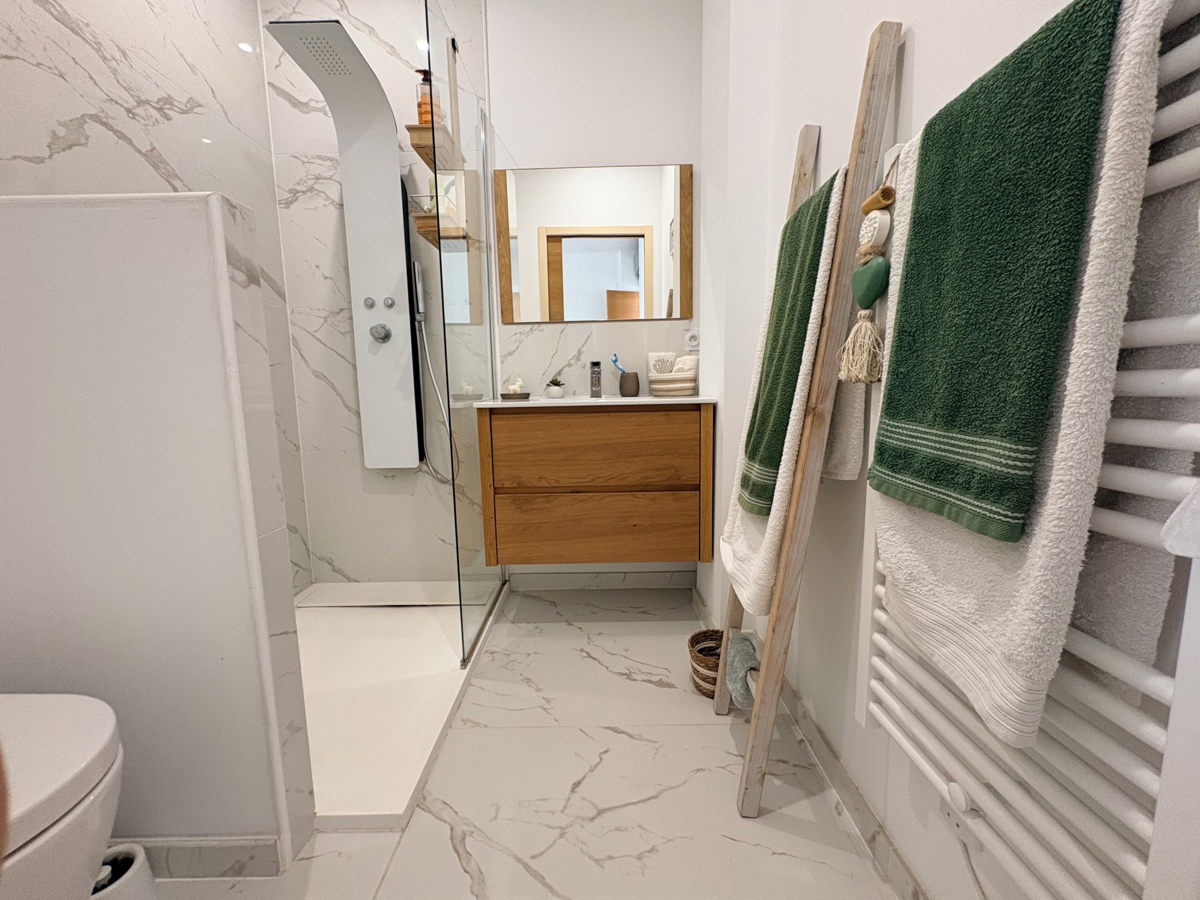 A bathroom with a shower, a toilet, a vanity with a mirror, and towels on a rack.