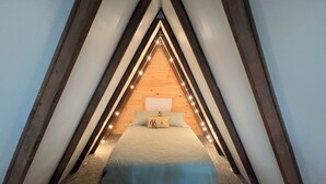 Un dormitorio abuhardillado triangular con cama, almohadas y luces colgantes.