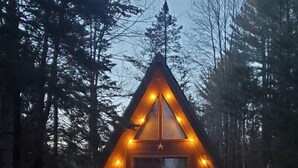Una cabaña con techo triangular, un porche con sillas e una bandera.
