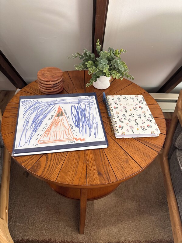 A round wooden table with a notebook, a sketchbook, and a small potted plant.