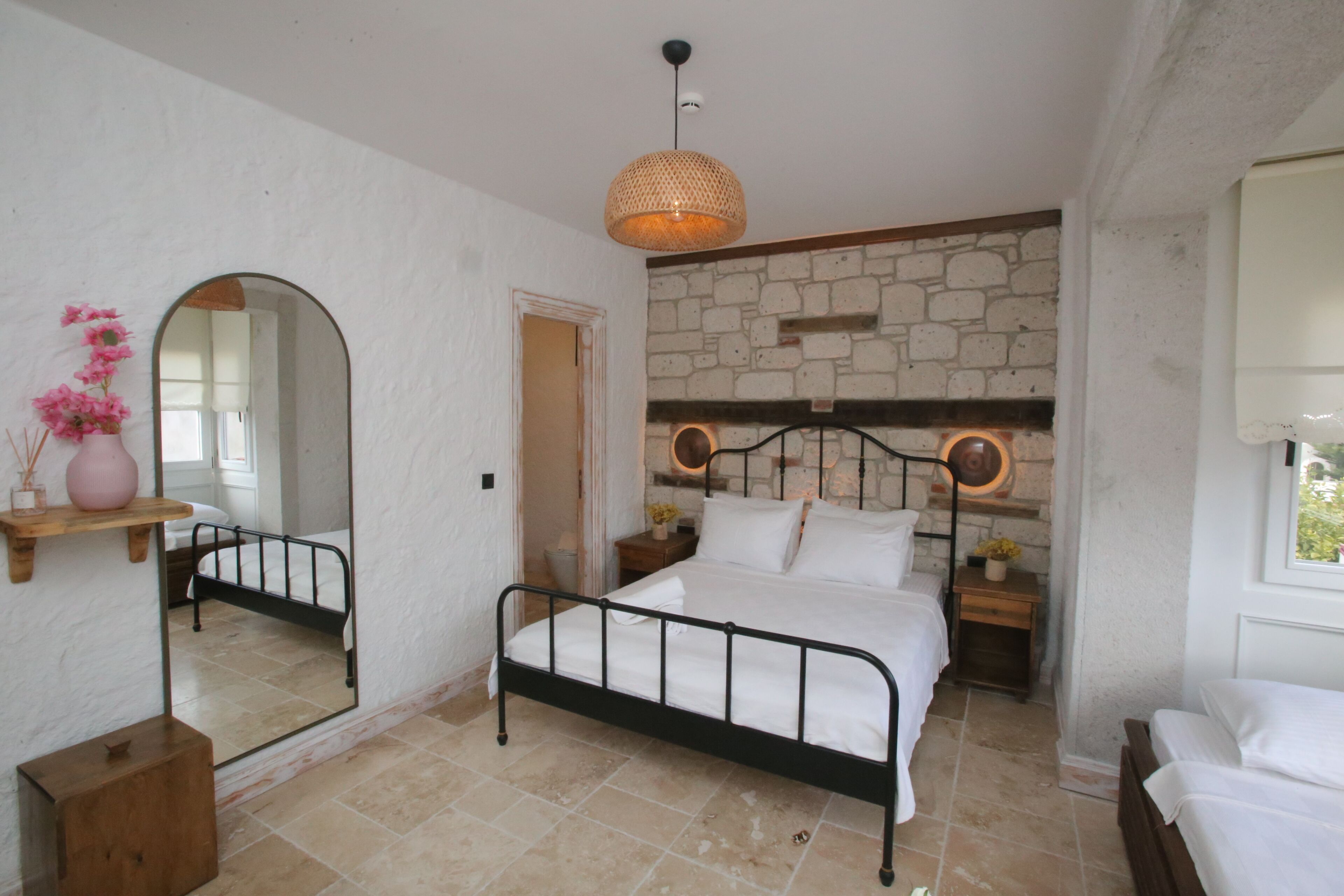 Un dormitorio con pared de piedra, una cama, una mesita de noche, un espejo y una lámpara colgante.