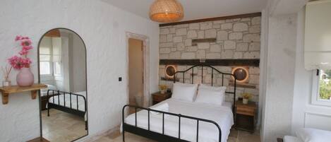 Un dormitorio con pared de piedra, una cama, una mesita de noche, un espejo y una lámpara colgante.