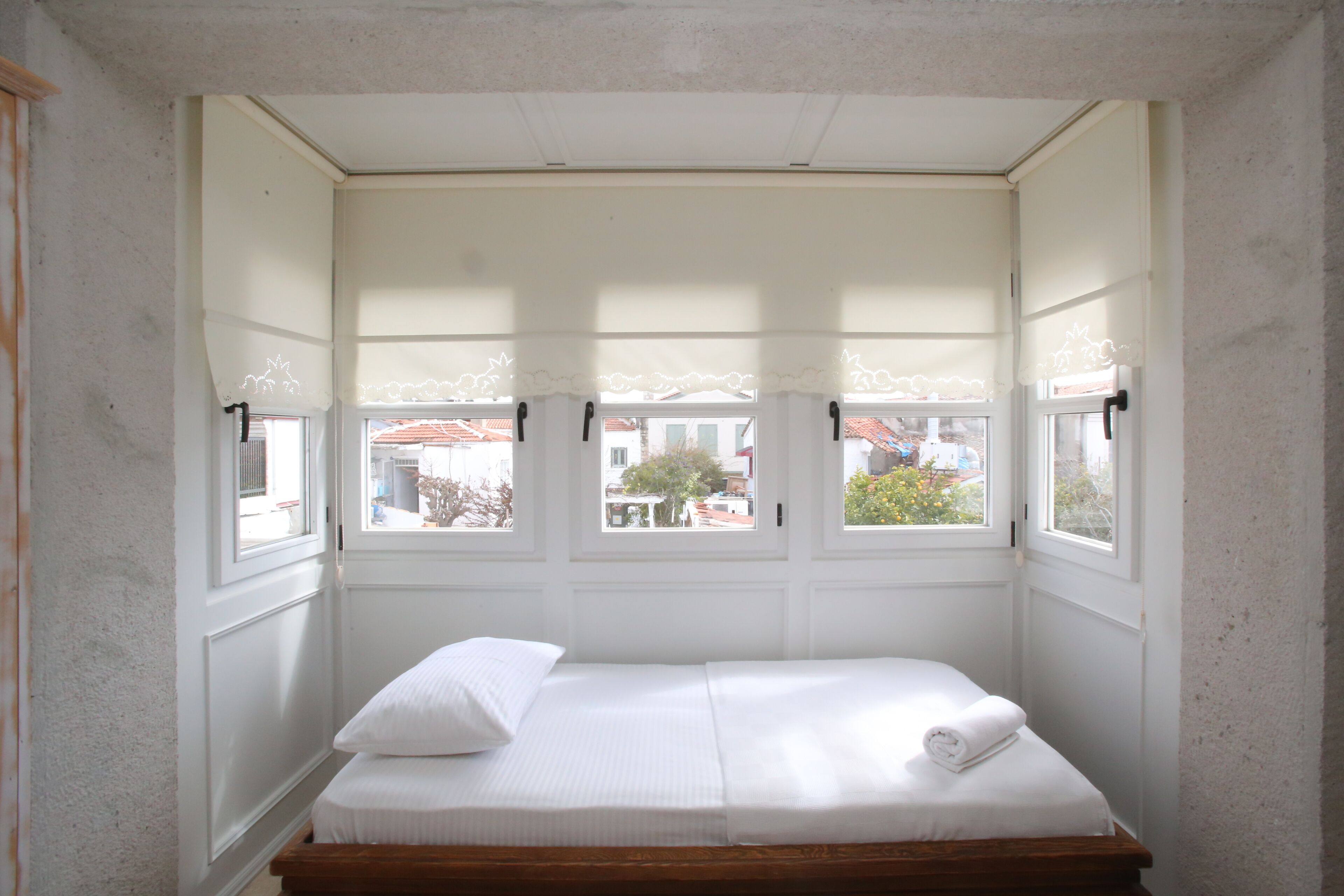 A small, single-bed room with a windowed bay window, white walls, and a wooden headboard.