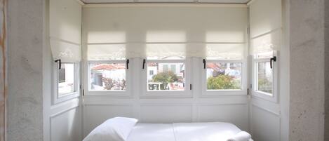 A small, single-bed room with a windowed bay window, white walls, and a wooden headboard.