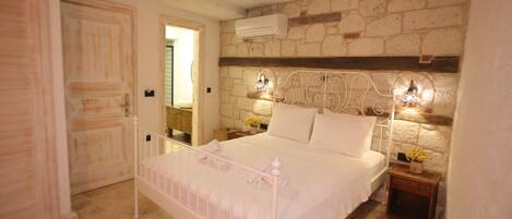 A bedroom with a stone wall, a bed with white bedding, two bedside tables with lamps, and a hanging light fixture.