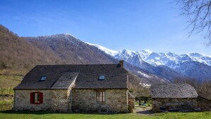 Un bâtiment en pierre avec un toit en pente, une petite fenêtre et un volet rouge.