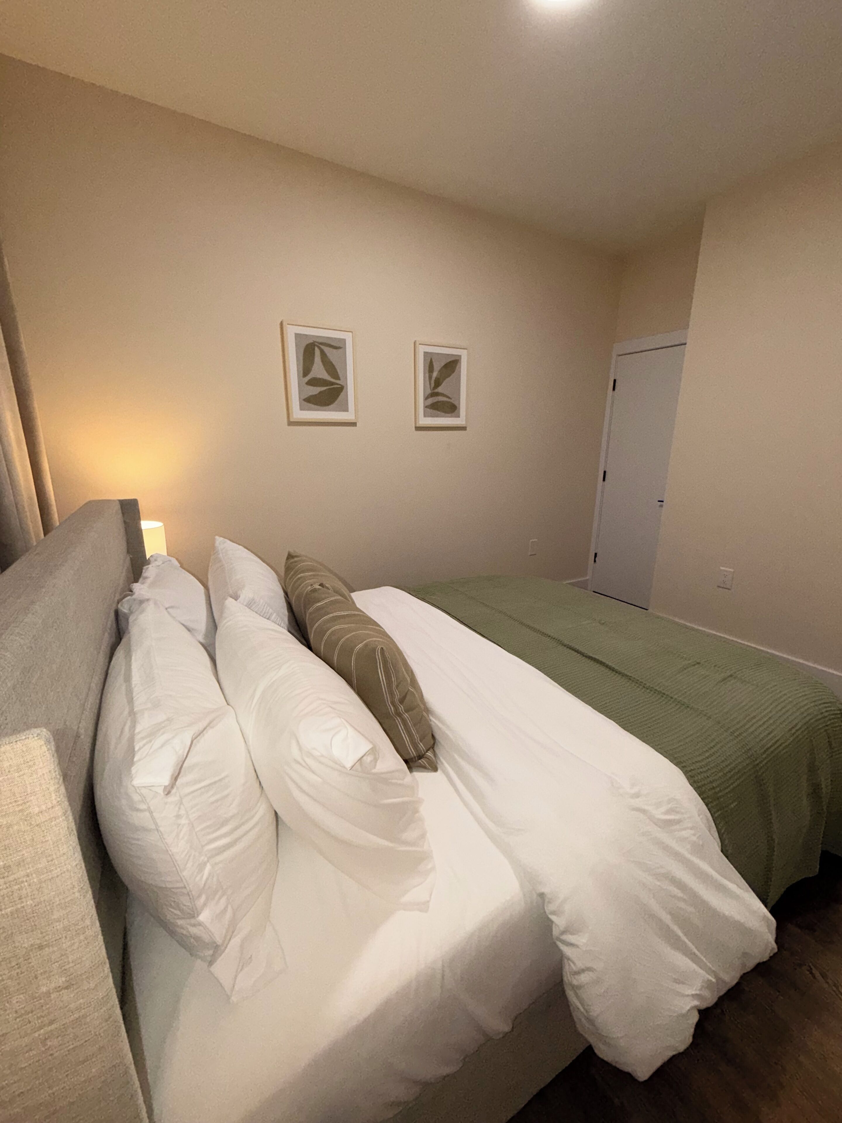 Quarto com cama, almofadas, abajur e duas fotografias emolduradas na parede.