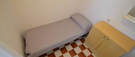 Una habitación pequeña con piso a cuadros, una cama individual cubierta con un edredón blanco y un armario de madera.