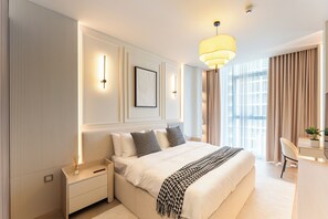 Moderni hotellihuone, jossa on suuri sänky, yöpöydät, työpöytä ja suuri ikkuna, jossa on verhot.