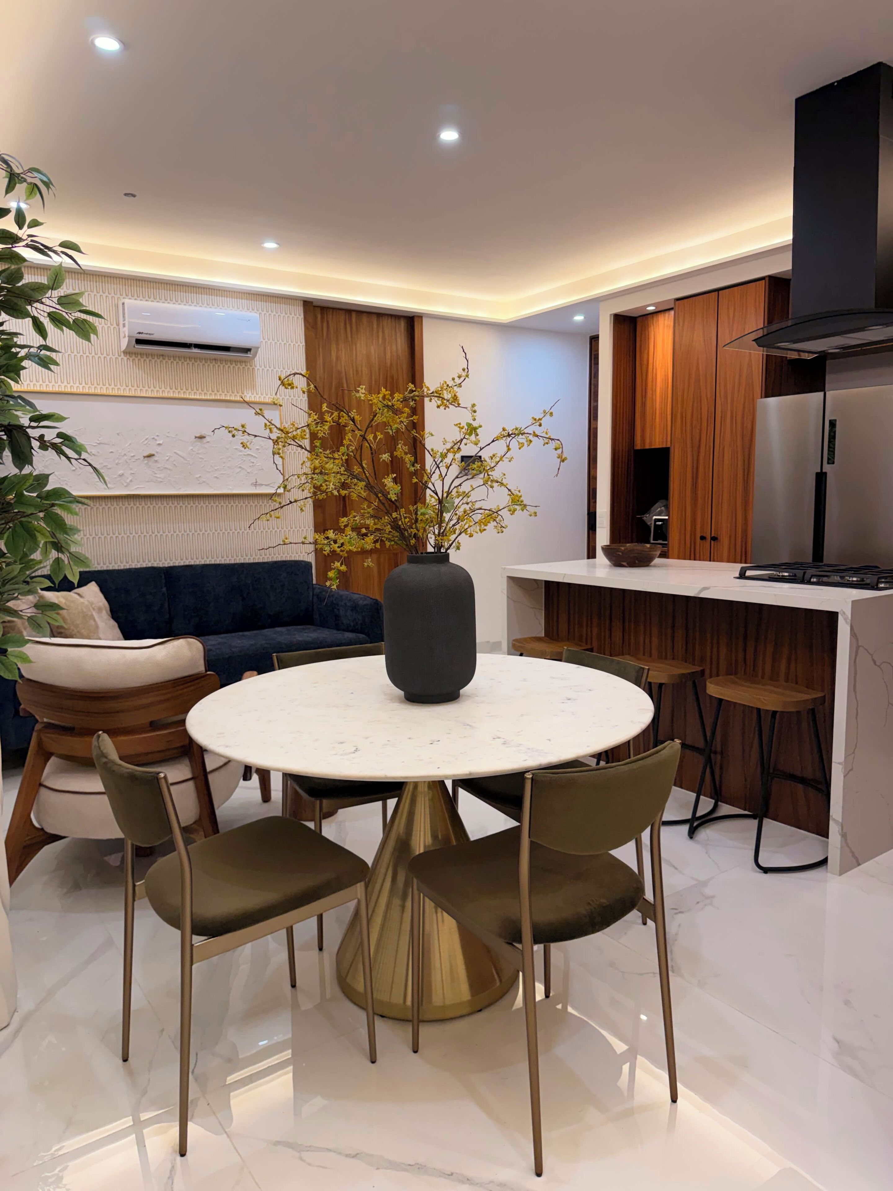 Une cuisine moderne dotée d’une cuisinière intégrée, un coin repas avec une table ronde et des chaises, et un canapé bleu en arrière-plan.