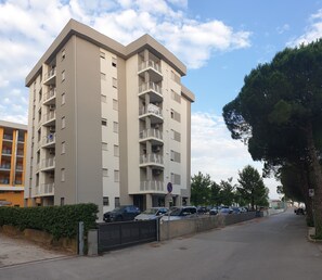 Un immeuble résidentiel à plusieurs étages, doté de balcons, d’un espace de stationnement et surplombant un ciel dégagé.