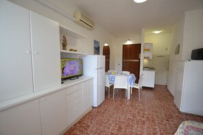 Une cuisine compacte avec des meubles blancs, un réfrigérateur, une table à manger avec des chaises et un téléviseur posé sur un meuble.