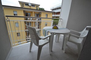 Un balcon avec des chaises et une table en plastique blanc, donnant sur un immeuble jaune doté de nombreux balcons.