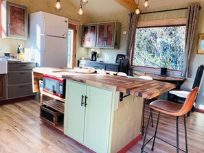 A kitchen with a central island, wooden cabinets, a refrigerator, and a window with a view of trees.
