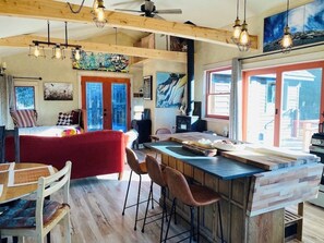 A spacious kitchen with a large island, wooden beams, and pendant lighting. - Artful and private cabin in Homer- 1 BR, close to town,  sleeps four (Homer)