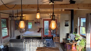 A cozy room with a bed, a sofa, and a wooden table. There are hanging lights and a ceiling fan.
