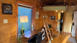 A wooden interior with a desk, chair, ladder, and a potted plant.