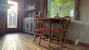 Un comedor con mesa y sillas de madera, una ventana con vistas a zonas verdes y una cocina con armarios y electrodomésticos.