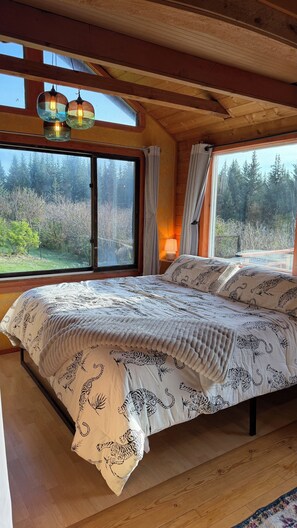 Une chambre avec un grand lit, un plancher en bois, une fenêtre avec des rideaux et une vue sur les arbres.