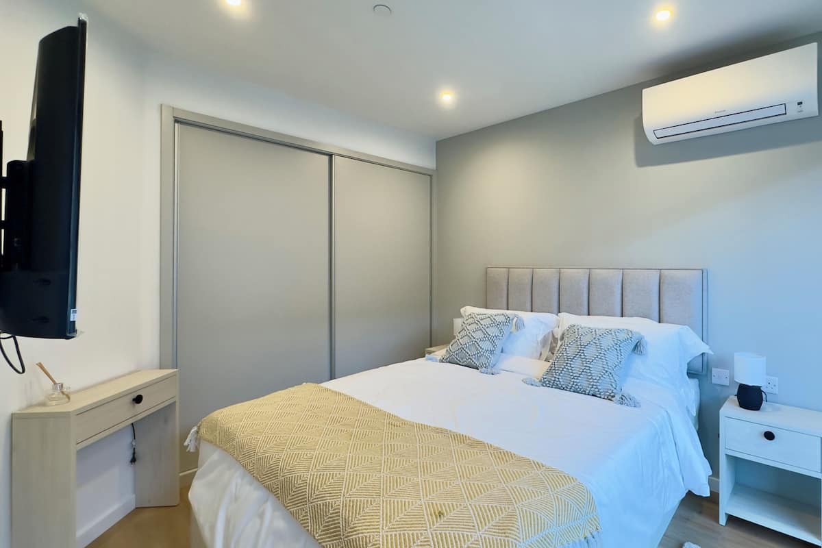 A bedroom with a bed, bedside table, nightstand, wall-mounted air conditioning unit, and a television.