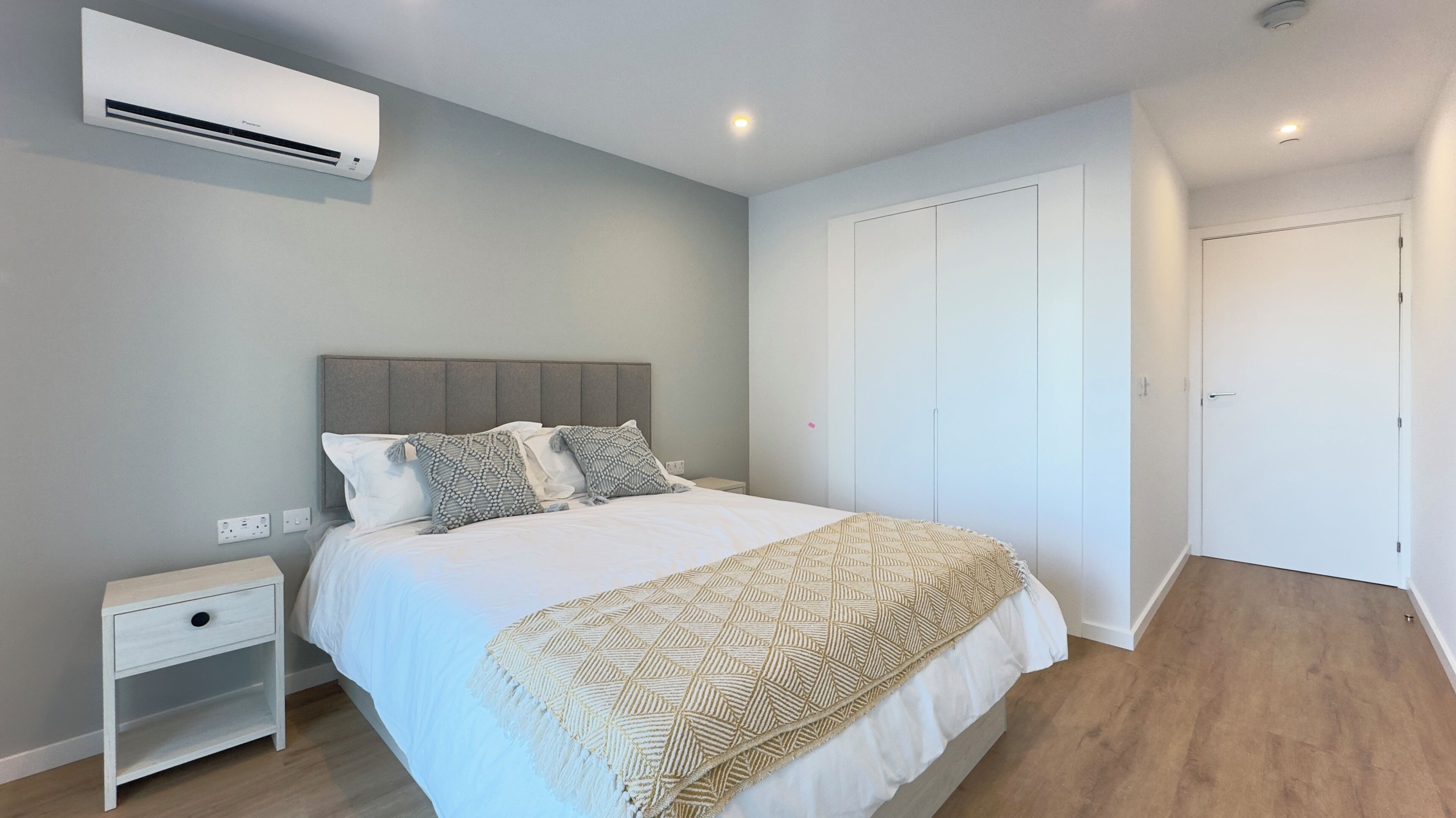 Un dormitorio moderno con cama, mesita de noche, armario y aire acondicionado integrado.