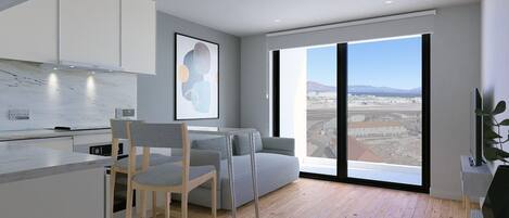 A modern kitchen with white cabinets, a dining area with a grey sofa and chairs, and a large window offering a view of a cityscape.