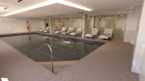 A swimming pool with lounge chairs, a tiled floor, and a marble wall. - Victory Suites (Gibraltar)