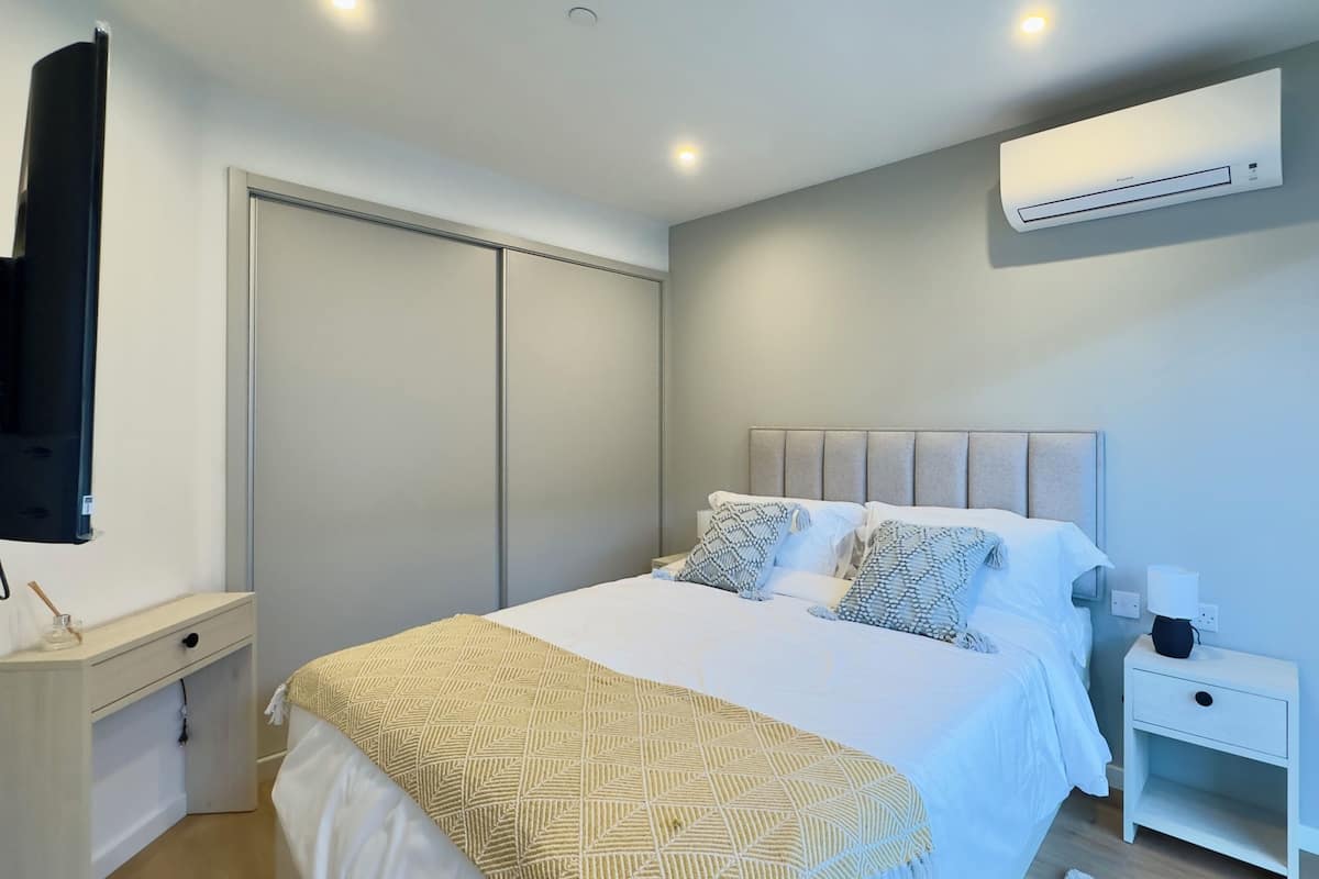A bedroom with a bed, bedside table, nightstand, wall-mounted air conditioning unit, and a television.