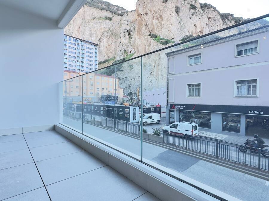 A balcony with a view of a street, buildings, and a cliff.