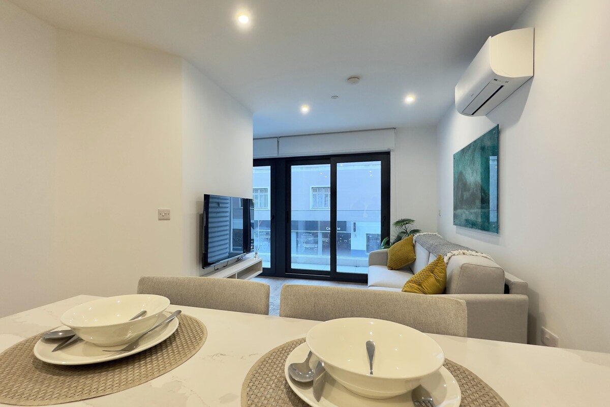A modern living room with a dining area, a sofa, a TV, and a large window.