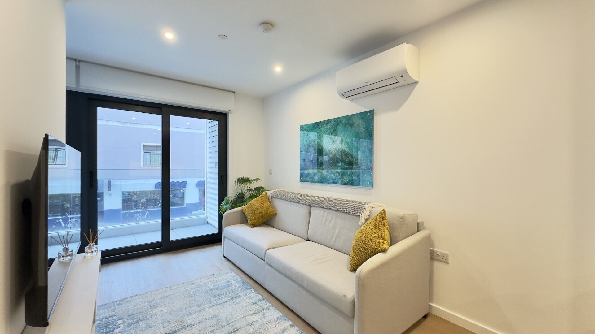 A modern living room with a sofa, a flat-screen TV, and a large window.