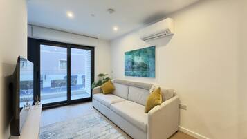A modern living room with a sofa, a flat-screen TV, and a large window.