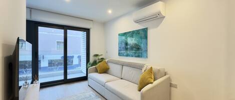 A modern living room with a sofa, a flat-screen TV, and a large window.