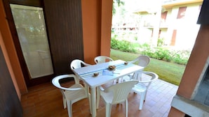 A patio with a table and chairs, a tiled floor, and a view of a building and greenery.