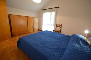 A bedroom with a large bed, a wardrobe, a chair, and a window with curtains.