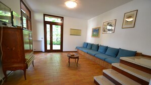 A living room with a sofa, a wooden cabinet, a small table, and a staircase. - Villa With Garden Near the Beach (San Michele al Tagliamento)