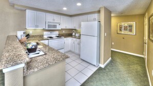 A compact kitchen with white cabinets, a microwave, a refrigerator, and a granite countertop. - NCAA - Walk to Daytona Beach Bandshell - Ocean Walk - 1 BD (Daytona Beach)