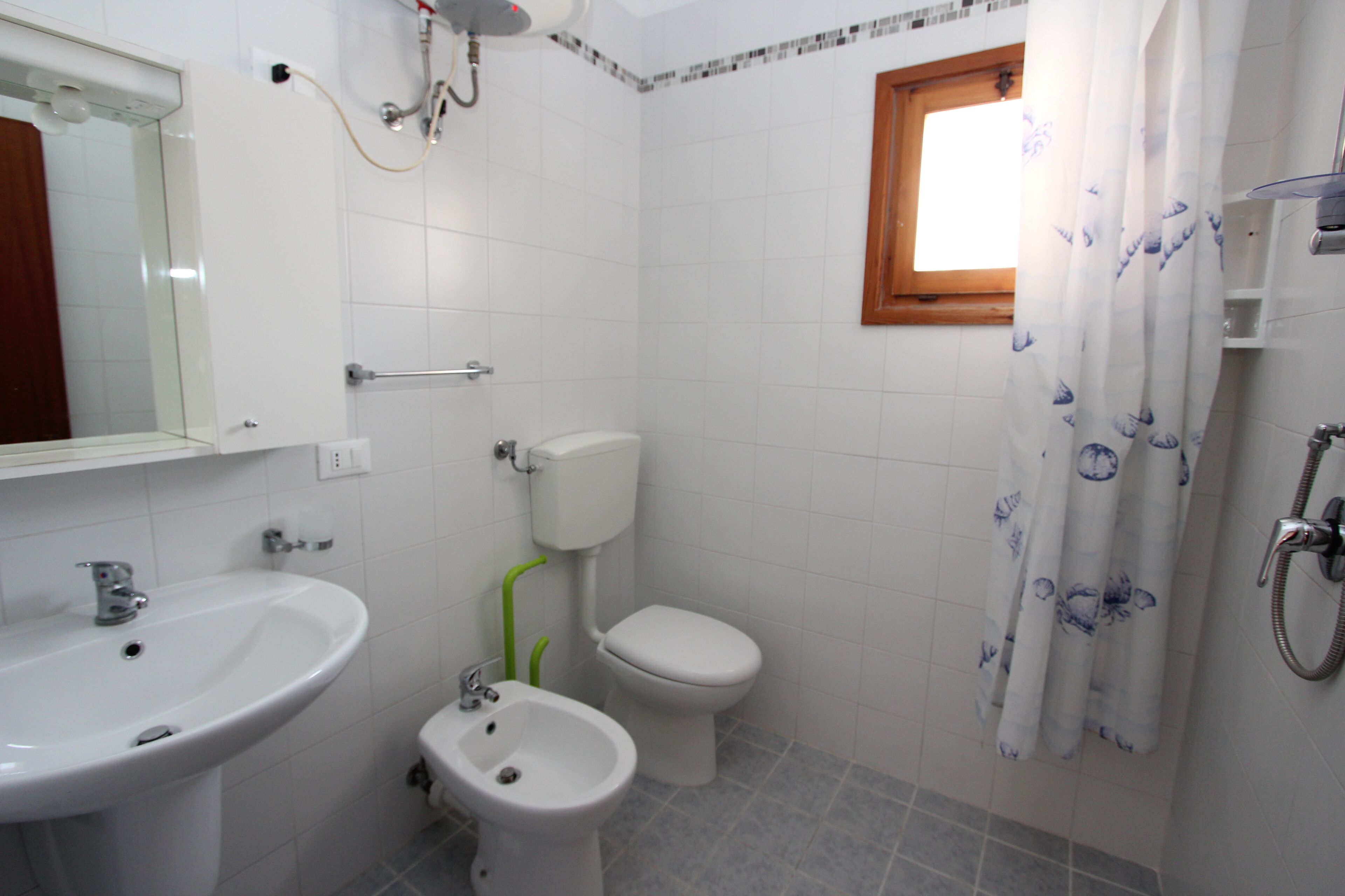 Baño con lavamanos, bidé, inodoro, ducha y ventana con cortina.