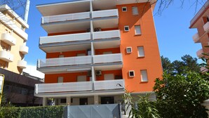 Un edificio a più piani con balconi, cielo sereno e vegetazione circostante.