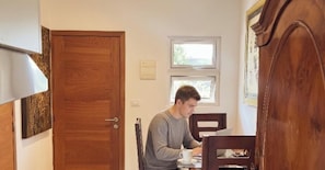 A person sitting at a table with a cup, a window above, and a door to the left. - Habitat Samaná Apartments - Las Galeras x2 (Las Galeras)