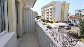 A balcony with a view of a multi-story building with balconies, a parking area, and a clear sky. - Comfy Apartment in Bibione (San Michele al Tagliamento)