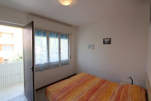 Een slaapkamer met een bed, een raam met gordijnen, een deur en een klein schilderij aan de muur.