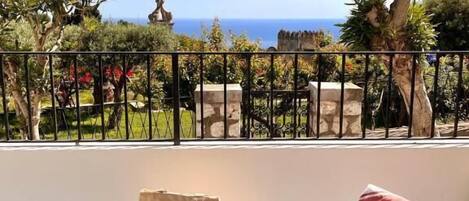 A balcony with a view of the sea, a table with a plant, a bag, and a striped cushion.